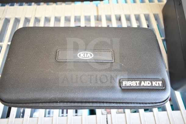 Kia first aid kit with branded case, part of 9-item auction lot, including Hyundai, Nissan, Genesis kits, and VW roadside kit.