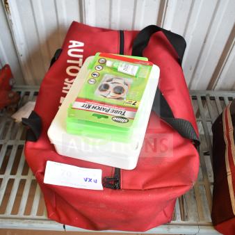 Red auto safety bag with a Slime Tube Patch Kit and white Cintas first aid kit on top, against a metal wall. Signs of wear.