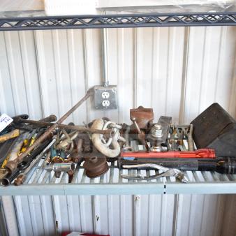 Assorted tools and items including flashlights, hitches, and wrenches on a shelf. Includes rusted and used conditions.