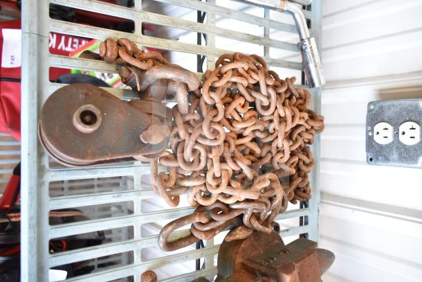 A pile of rusty chains and a metal pulley on a metal shelf, part of an auction lot with tools and flashlights.