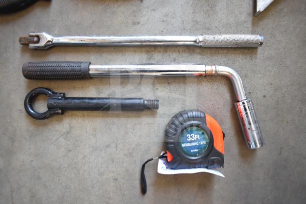 Assorted tools including a wrench, 33ft measuring tape, hitch, and grip bars. Good condition with visible wear.