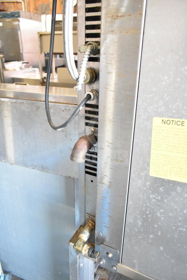 Baxter commercial gas mini rotating rack oven in stainless steel, visible piping, and notice label. Mounted on casters.
