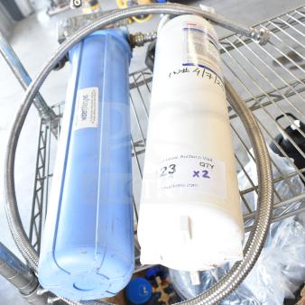 Water filtration system with blue and white filters, metal hose, and labels indicating auction details. Good condition.