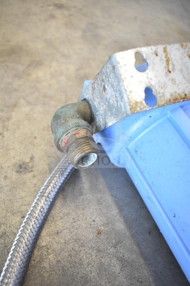 Water filtration system with blue housing, metal connector, and braided hose. Some rust and wear visible on the bracket.