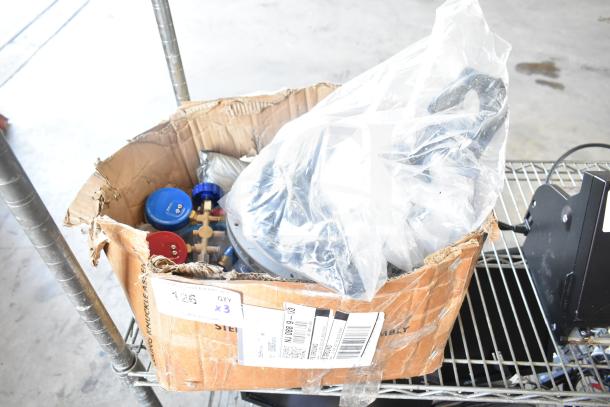 Lot of various items including gauges, hoses, metal pieces in a worn cardboard box, with shipping labels visible.