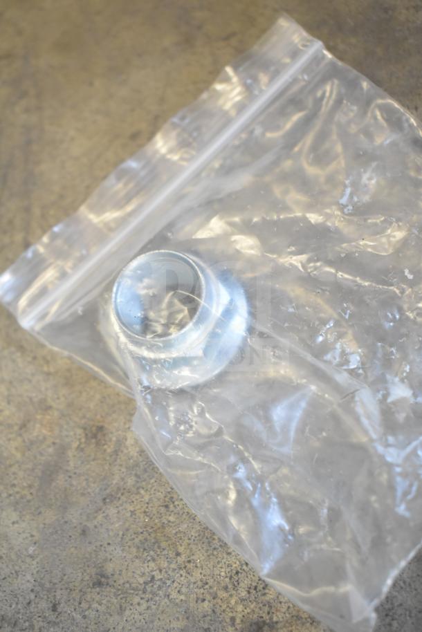 Clear plastic bag with a small metal piece inside, part of a mixed lot including gauges, hoses, and other metal items.