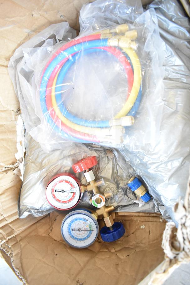 Lot of assorted items including red, blue, yellow hoses, dual pressure gauges, and metal connectors in a cardboard box.