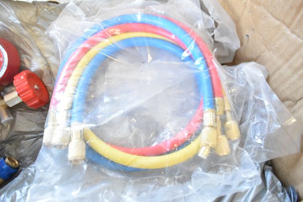 Colorful hoses with brass fittings, wrapped in plastic, part of a mixed lot including gauges and metal pieces.