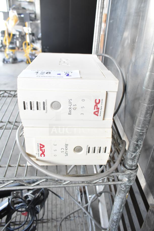 Two APC Back-UPS CS 350 units on a metal shelf, showing power and indicator labels. Slightly worn condition.