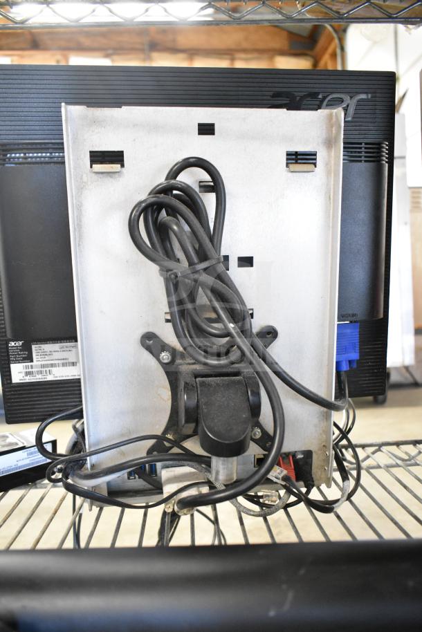 "Back view of two Acer monitors with connected cables, featuring an NCR kitchen controller attached. Labels visible on the monitor backs."