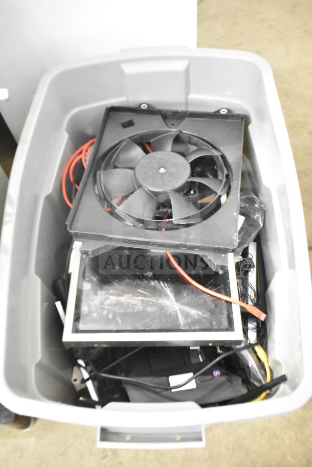 Gray bin containing various electronics including Kitchen Armor monitor, Netgear router, PlayStation controllers, and cables.