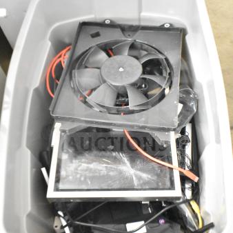 Gray bin containing various electronics including Kitchen Armor monitor, Netgear router, PlayStation controllers, and cables.