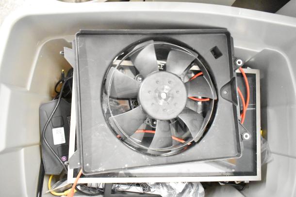 Gray bin containing various electronics including a Kitchen Armor monitor, Netgear router, PlayStation controllers, and cables.
