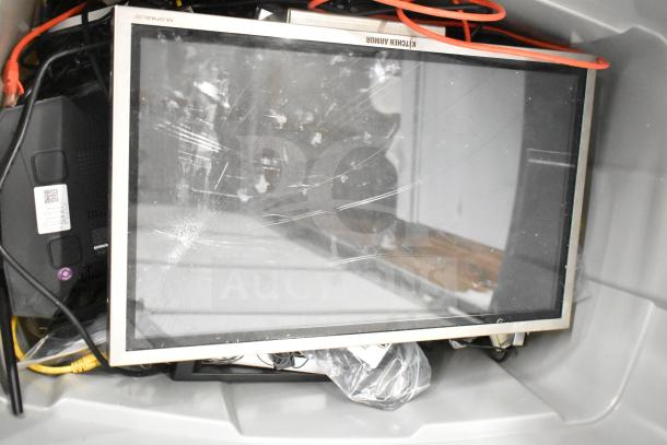 Gray bin containing a Kitchen Armor monitor with visible scratches, Netgear router, PlayStation controllers, and various cables.