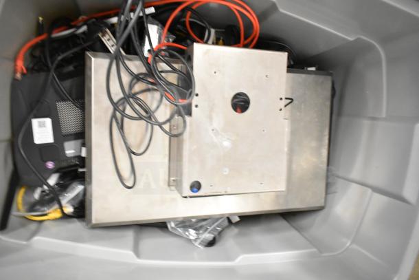 Lot of electronics in a gray bin, including a Kitchen Armor monitor, Netgear router, PlayStation controllers, and cables.
