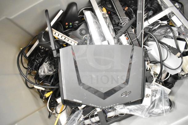 Lot of items in gray bin, includes Kitchen Armor monitor, Netgear router, PlayStation controllers, and assorted cables.