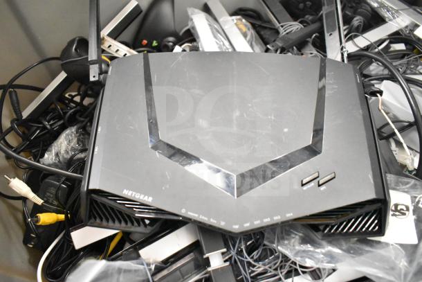 Lot including Netgear router, PlayStation controllers, cables in a gray bin; visible wear; tags and markings shown.