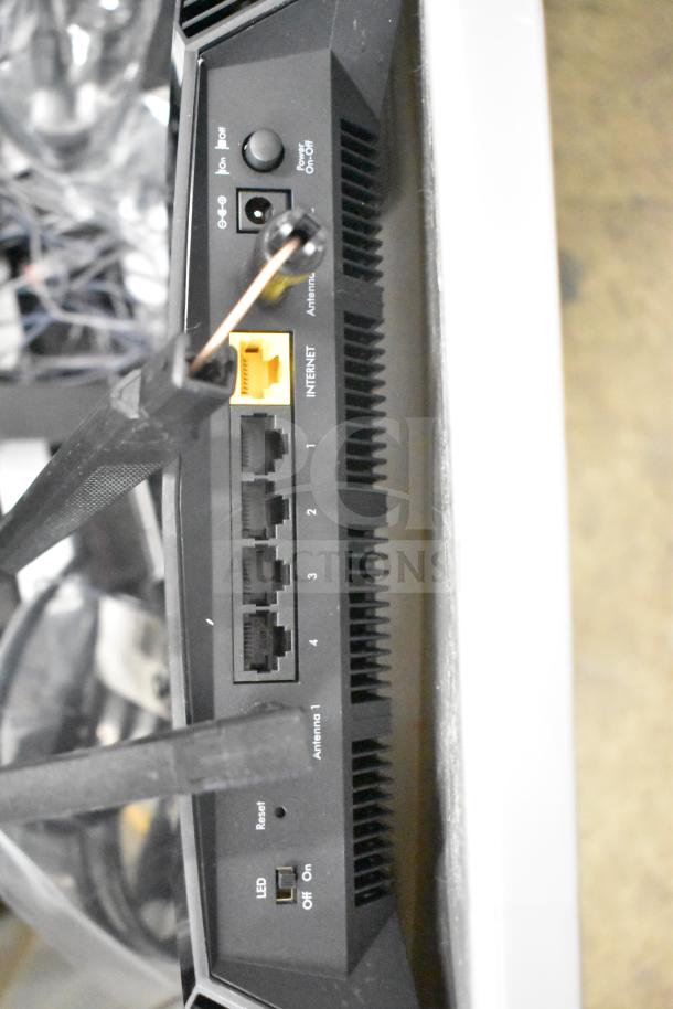 Lot of various electronics in gray bin including a Netgear router, PlayStation controllers, and cables.