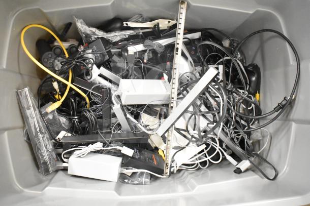 Gray bin with assorted tech items: Kitchen Armor monitor, Netgear router, PlayStation controllers, various cables. Mixed condition.
