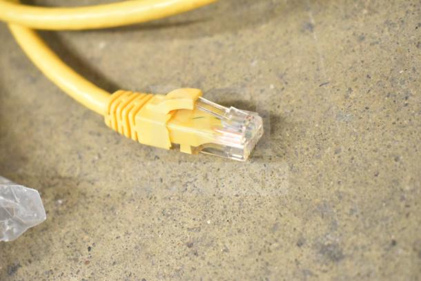 Yellow Ethernet cable with clear connector on concrete surface. Part of lot including Kitchen Armor monitor, Netgear router, PlayStation controllers in gray bin.