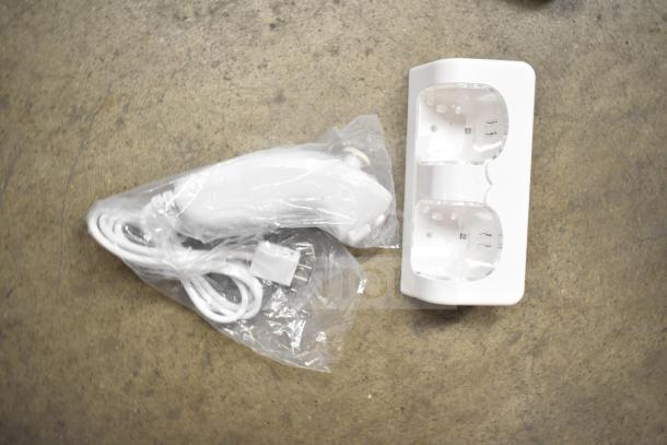 White PlayStation controller charging dock and USB cable on a concrete surface.