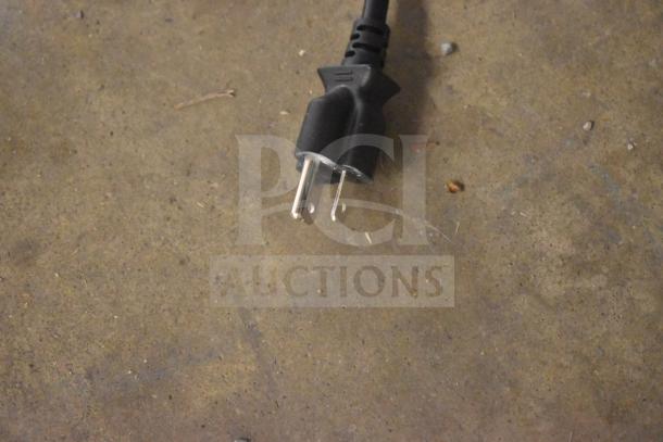 Close-up of a three-prong electric plug on a textured surface. Plug is part of a KoolMore vending machine.