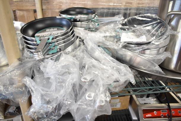 19 new scratch and dent Choice 8" aluminum non-stick fry pans, stacked with labels, partially wrapped in plastic.
