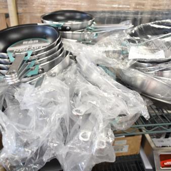 19 new scratch and dent Choice 8" aluminum non-stick fry pans, stacked with labels, partially wrapped in plastic.