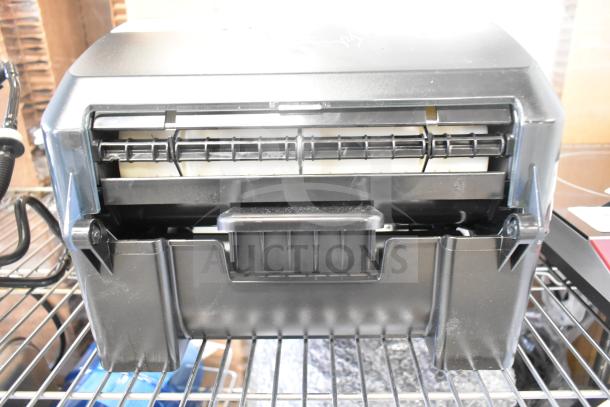 BRAND NEW Tork 772728 Black Mechanical Paper Towel Dispenser, H71, visible scratches, on metal shelving.