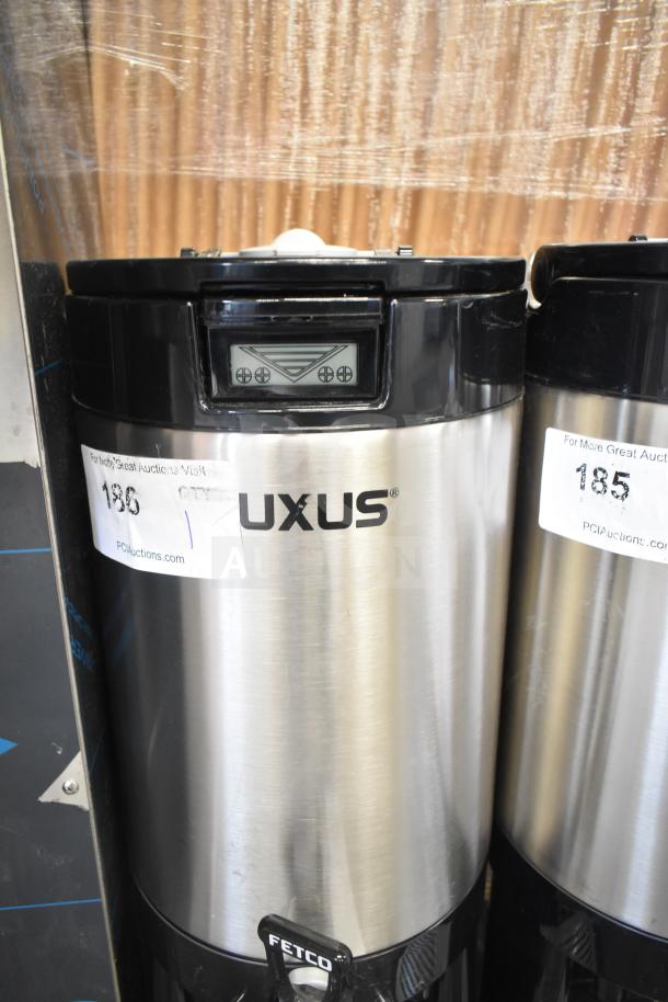 "Brand new Fetco L4D-20 Luxus 2-gallon stainless steel coffee server with stand, minor scratches, auction label visible."