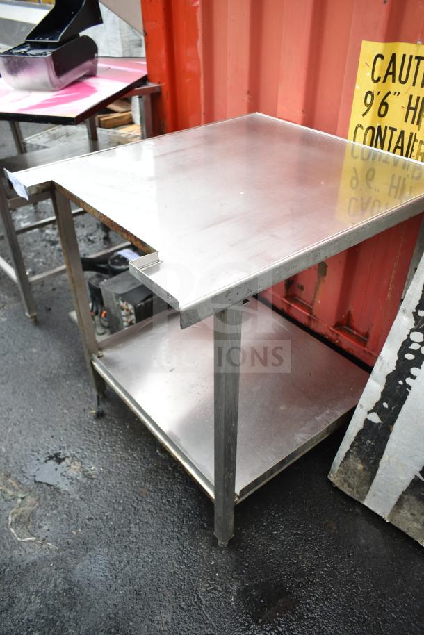 Stainless steel commercial table with under shelf, in used condition, featuring sturdy metal legs and a smooth surface.