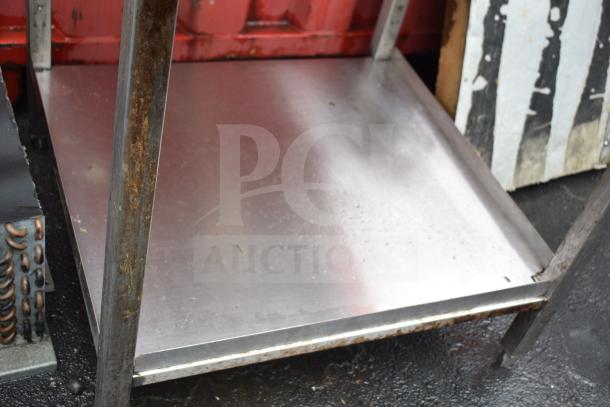 Commercial metal table with under shelf, sturdy construction, visible rust on legs, used condition.