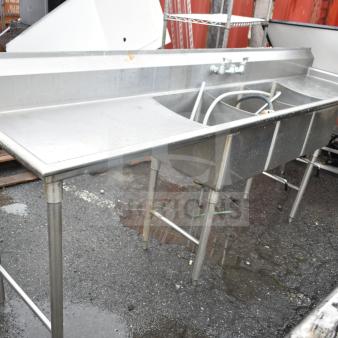 Commercial 3 bay sink with dual drain boards, stainless steel, used condition, visible faucet and plumbing attachments.