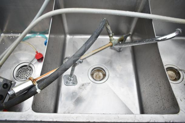 Commercial 3 bay sink with dual drain boards, stainless steel, visible plumbing connections, lightly worn condition.