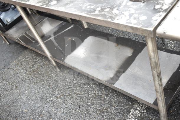 Commercial stainless steel table with under shelf, showing signs of use. Sturdy construction, ideal for kitchen or workspace.