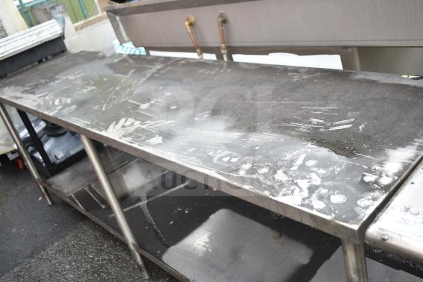 Stainless steel commercial table with under shelf, showing wear, suitable for kitchen or industrial use.