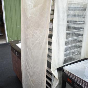 Pan transport rack with baking pans, covered with a protective drape. Visible wear on the cover. Multiple shelving units.