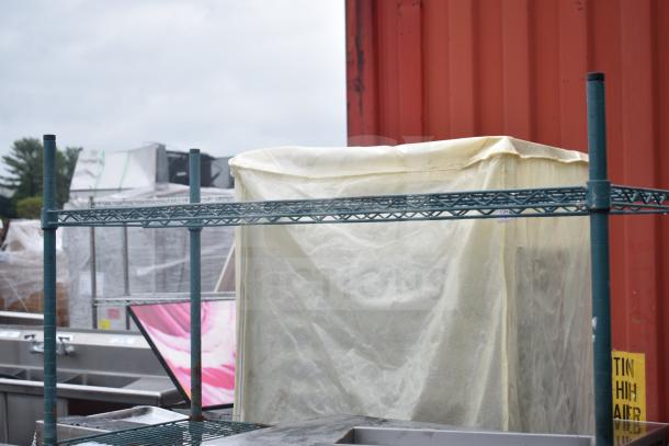 Four-tier green wire shelving unit on commercial casters, partially covered, includes contents. Buyer must dismantle.