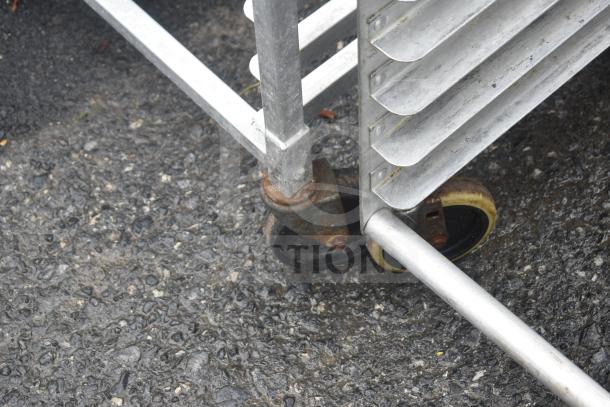 Commercial pan transport rack on heavy-duty casters, metal construction, slightly rusted, outdoor setting.