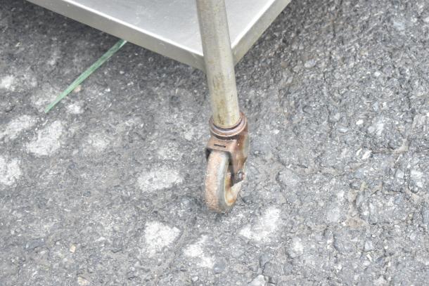 Commercial table caster on asphalt, showing metal frame corner. Rust present on caster, indicating use.