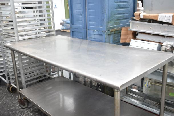 Commercial table with under shelf on casters, stainless steel, showing moderate wear. Ideal for industrial use.