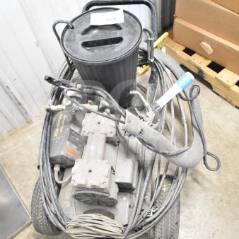 CapSpray compressor/pump with attached hoses and handle, showing wear, on wheels. Dusty surface, label partially visible.