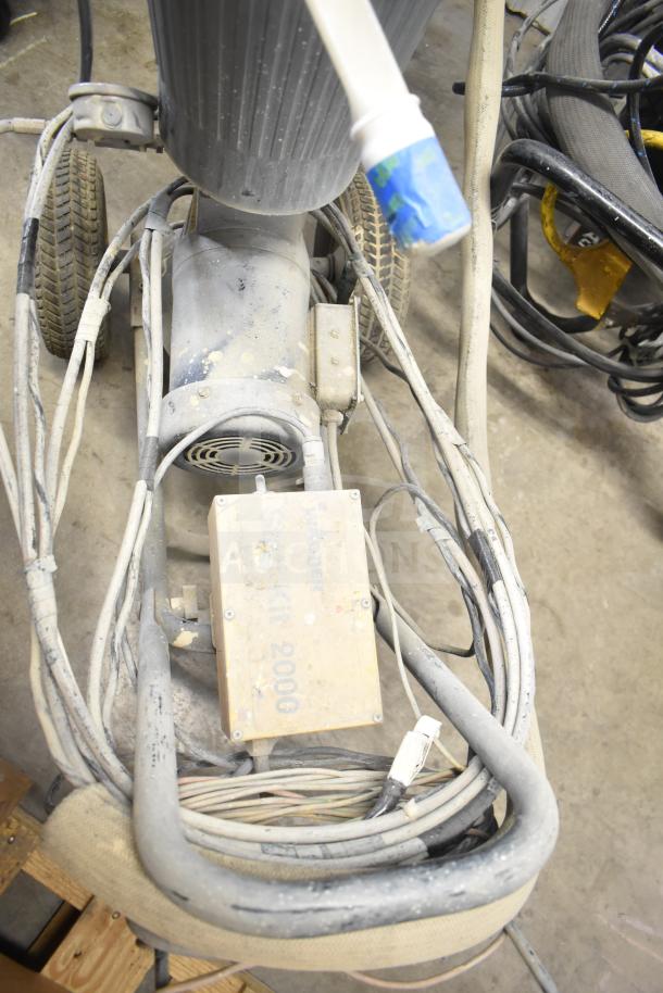 SprayTech 1075 Airless Spraying System, used condition, visible surface wear, equipped with hoses and mounted on wheels for mobility.