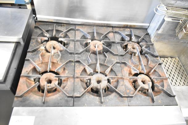 Montague Grizzly commercial gas-powered 6-burner range with oven, featuring a stainless steel backsplash, showing signs of use.