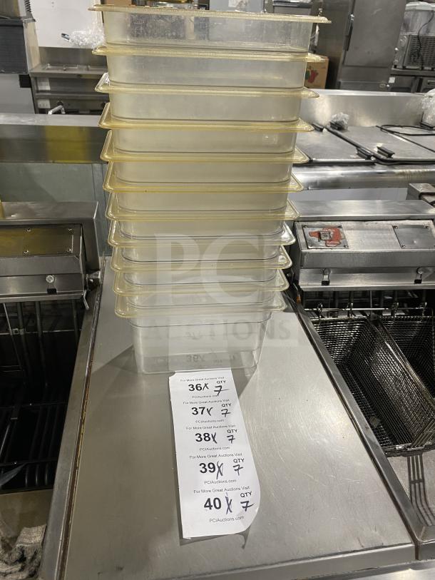 Stack of commercial clear polycarbonate food pans on a kitchen counter, includes paper tag with bid details, quantities marked.
