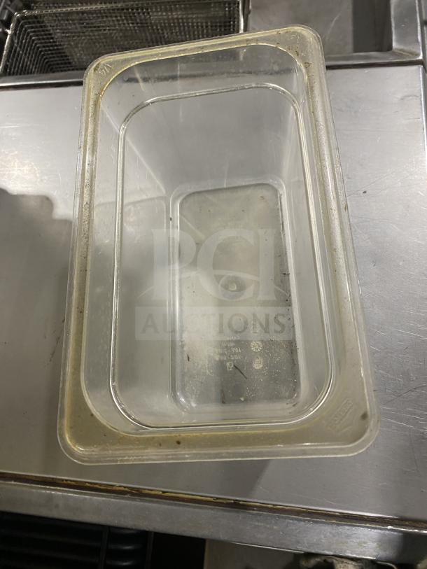 Clear polycarbonate commercial food pan, rectangular, slightly worn, visible markings for measurement and brand.