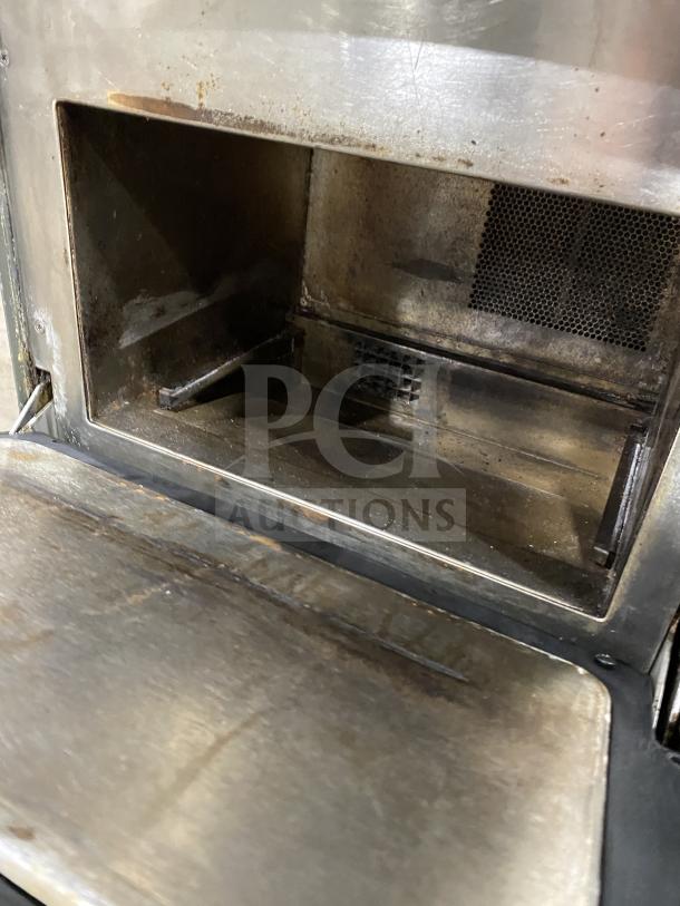 Metal wood stove interior showing signs of use, with ash residue and darkened surfaces. Features a mesh vent and worn metal.