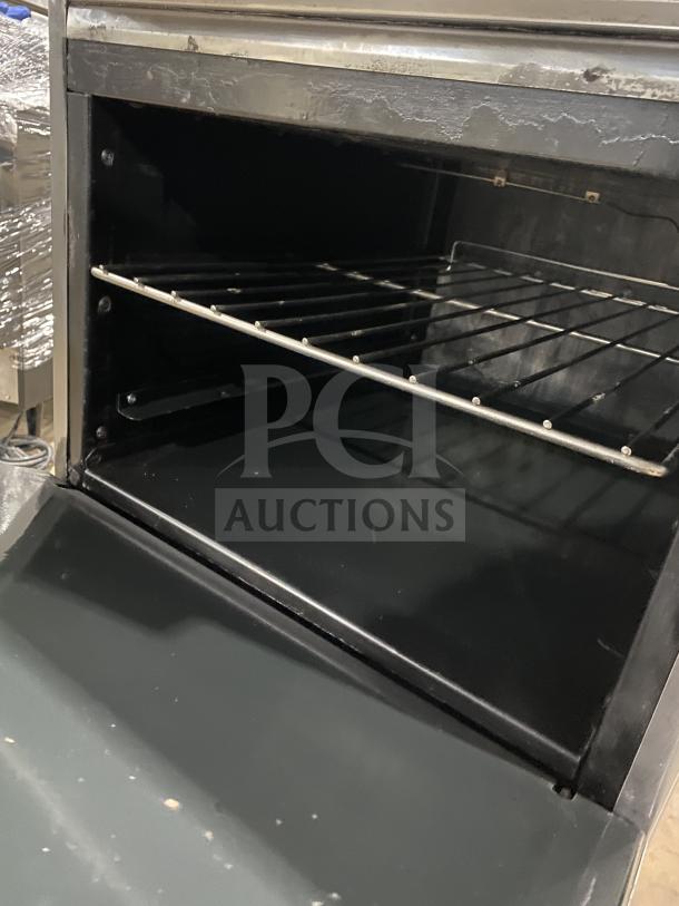 American Range commercial stainless steel 4-burner range/oven combo with backsplash, overhead salamander shelf, and wired oven rack on casters.
