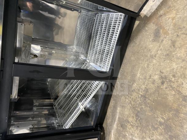Commercial back bar black refrigerator with poly coated wired rack and two sliding glass doors, in good condition.