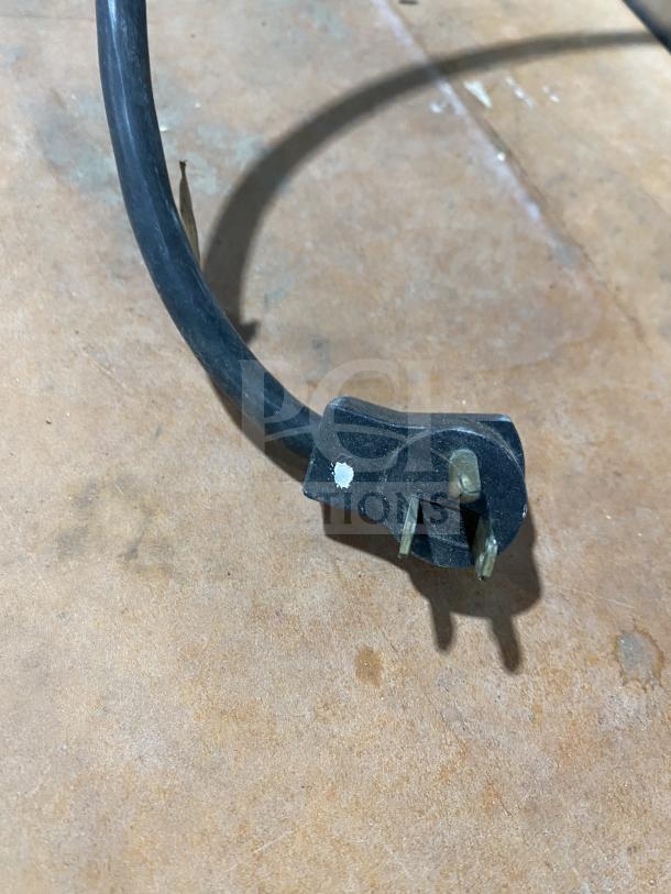 Power plug for Delfield refrigerated prep table, showing three-prong design and black cable on a wooden surface.